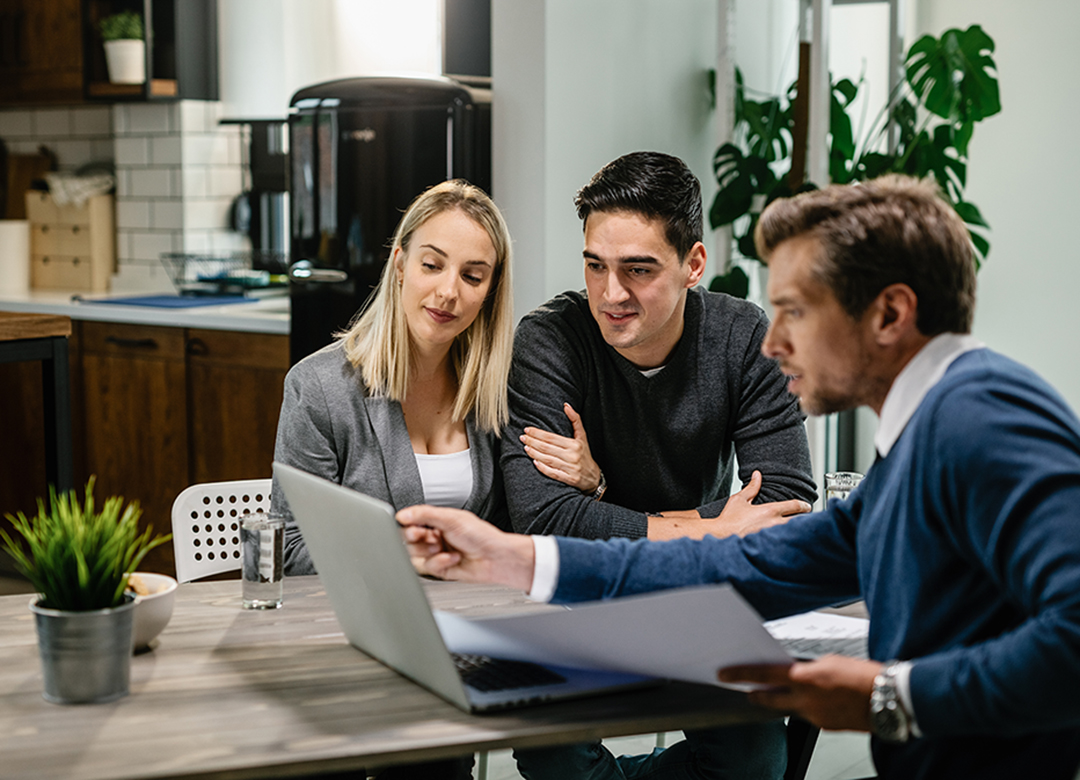 Smiling couple using a computer with their investment agent on a meeting.